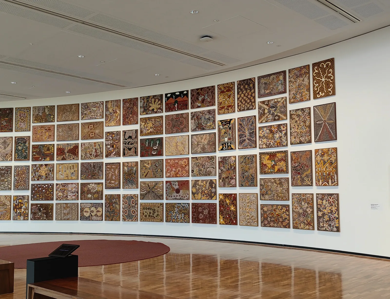 Salon hang of 81 Emily Kam Kngwarray paintings on a curved white gallery wall at the National Gallery of Australia