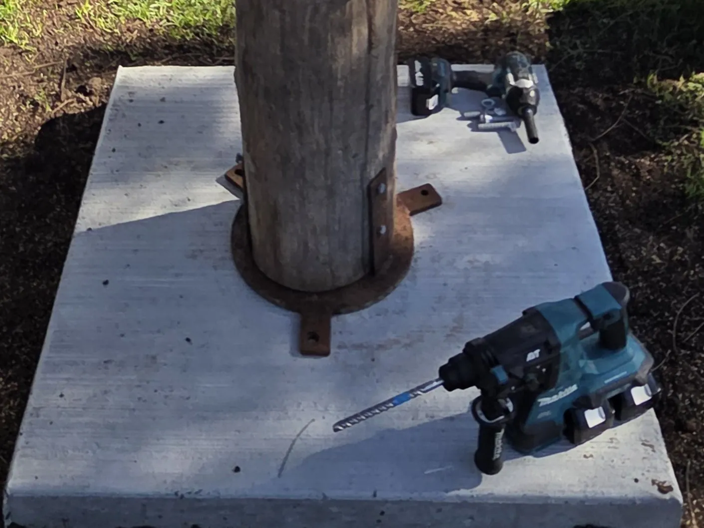 Sculpture footing: timber post fixed into a steel base plate on a new concrete pad, drills beside it